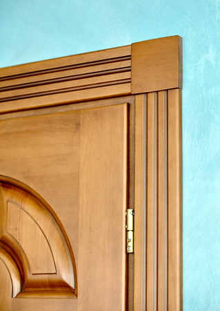 Element of wooden door in frame of brown wood carved geometric ornaments classical style with gilded hinges on blue plastered wall background close upの写真素材