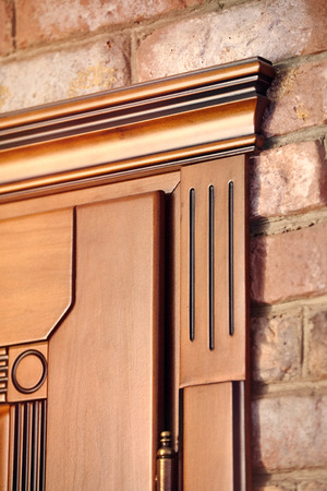 Element of a wooden door brown colored carved in classical geometric style with golden hinges on brick wall backgroundの写真素材