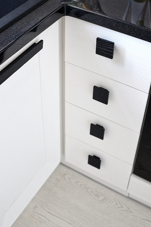 Solution for a kitchen corner storage in a cupboard. A corner unit with shelves and drawers with black square wooden handles and white brushed oak panels for utensils and kitchen accessories or spiceの写真素材