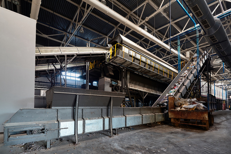 Conveyor belt at recycling plant transports garbage inside drum filter or rotating cylindrical sieve with trommel or screen for sorting pieces of garbage into fractions of various sizes.の写真素材