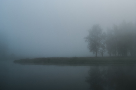 Early summer morning fog on river. Island, overgrown with wood, barely visible in dense fog. Thick morning mist brings depressive dull sinister state.の写真素材