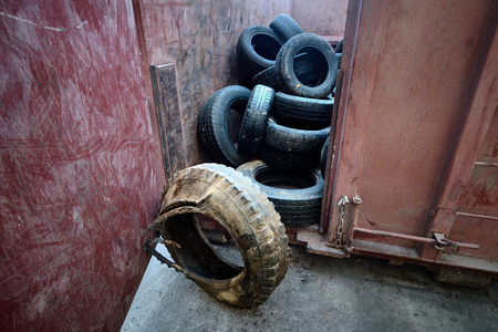 Old used obsolete car tires from trucks and passenger cars stored in metal container at waste recycling plant after sorting for further processing.の写真素材