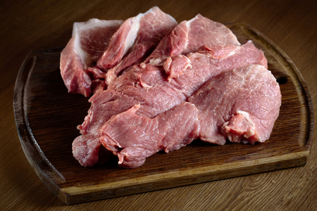 Raw pork on cutting board. Fresh pig meat steak slices on wooden cut board over oak table background close-up.の写真素材