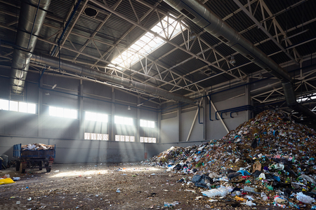 Modern plant for processing and sorting of municipal urban waste - evening sunlight in huge reception junkyard room, hangar for unloading waste from trucks and further processing sorting and reuse.の写真素材