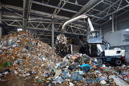 GRODNO, BELARUS - OCTOBER 2018: recycling plant process of uploading garbage to conveyor . Manipulator with grabber uploads waste on conveyor for further processing and sorting.のeditorial素材