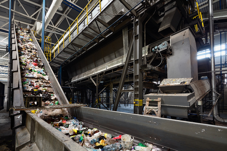 Conveyor belt at recycling plant transports garbage inside drum filter or rotating cylindrical sieve with trommel or screen for sorting pieces of garbage into various sizes fractions.の写真素材