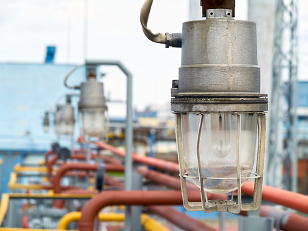 Row of lighting masts with lanterns in explosion-proof and fire-proof design close-up over background of pipelines buildings and equipment of chemical plant with copy space.の写真素材