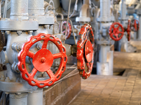 Red valves and latches on background of gray pipelines and compressors of chemical plant.の写真素材