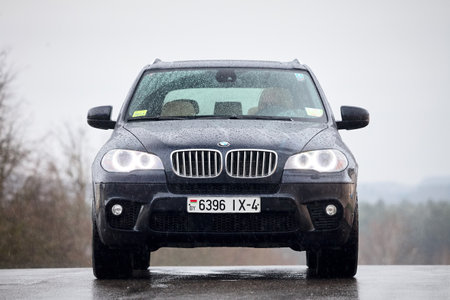 GRODNO, BELARUS - OCTOBER 2016: BMW X5 with glowing headlights standing on asphalt under rain covered with raindrops over gray rainy sky and forest background.のeditorial素材