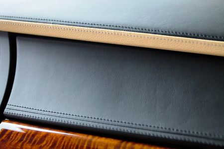 Part of the interior of expensive luxury car. Genuine leather gloves box panel in black and beige color stitched and varnished wood.の写真素材