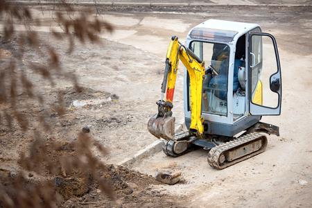 Tracked mini excavator breaks out old curbs before installing new curbs. The concept of using economical and compact equipment for urban needs.の写真素材