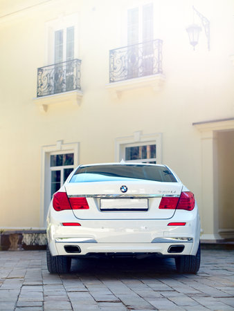 Grodno, Belarus, May 16, 2013: Modern luxury BMW 750Li XDrive car rear back view parked on stone paved parking near ancient house with balconies with wrought iron grilles  with sunflares.のeditorial素材
