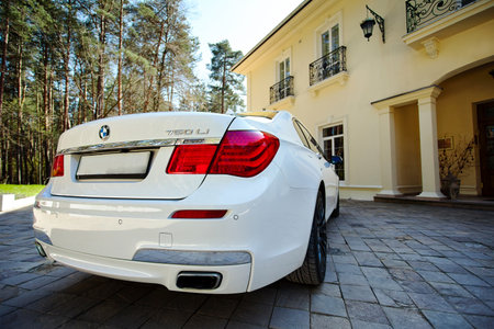 Grodno, Belarus, May 16, 2013: Modern luxury BMW 750Li XDrive car rear back close-up view parked on stone paved parking near ancient house with balconies with wrought iron grilles.のeditorial素材