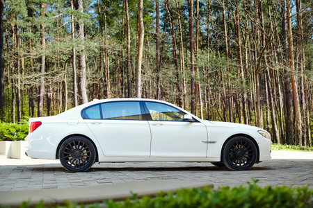 Grodno, Belarus, May 16, 2013: Modern luxury BMW 750Li XDrive car three-quarter side view parked on stone paved parking near pine forest.のeditorial素材