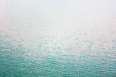 Texture of transparent clear surface of turquoise azure water with small ripples fish and sun reflections textured with waves background with copy space.の写真素材