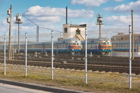 Wire fence restricting access to train depot with standing trains out of focus railway depot background. Concept of protecting strategic objects from unauthorized access.の写真素材