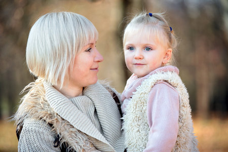 Smiling mother and daughter together in sunny park in autumn as happy family.