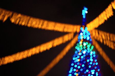 Christmas tree blurred image with multicolored lights and garlands out of focus over dark night background with copy space.の写真素材