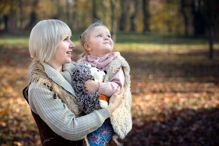 Smiling mother and daughter looking up together in sunny park in autumn as happy family.の写真素材