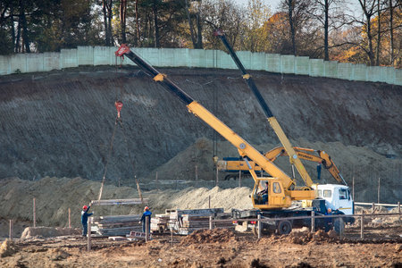 GRODNO, BELARUS - OCTOBER 2019: Workers with crane in safety protective equipment installing concrete floor slab panel at building construction site.のeditorial素材