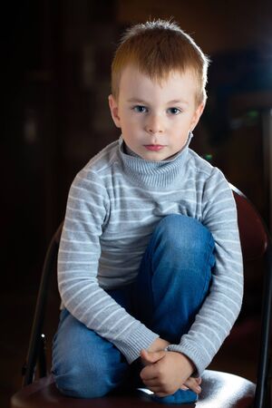 Portrait of dreamy pensive blond boy with gaze his eyes over dark background with specks of dust flying in backlight with flares and copy space.の写真素材