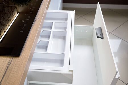Solution for placing kitchen utensils in modern kitchen - horizontal sliding pullout drawer shelves storage in cupboard for kitchenware cookware under oak countertop with induction hobの写真素材