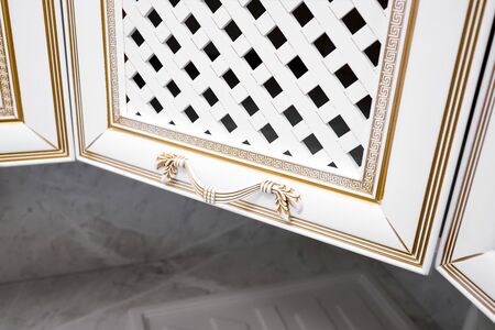 Concept of door handle furniture. Decorative element of kitchen facade panel knob of white wooden kitchen cabinet or cupboard in white and gold ancient greek ornament border decoration patternの写真素材