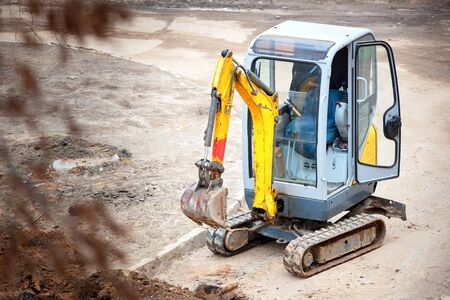 Tracked mini excavator breaks out old curbs before installing new curbs. The concept of using economical and compact equipment for urban needs.の写真素材