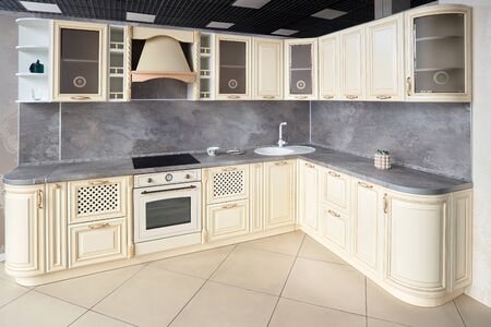 Interior of modern kitchen in classic style with golden elements in beige colors with built-in appliances electric or induction hob, electric oven stone sink and extractor fanの写真素材