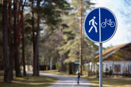 Bicycle and pedestrian shared route road sign over out of focus background of road in park surrounded by forest and housesの写真素材