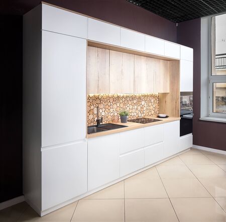 Luxury modern fitted flat design kitchen with surface behind the countertop decorated with wall cross section of tree trunks of cut tree logs, trunks placed together for interior decorationの写真素材