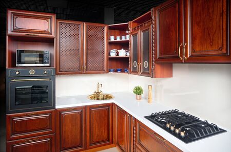 Interior of modern kitchen in classic style with golden elements cherry alder wood cabinetry with built-in appliances electric or induction hob, electric oven stone sink and extractor fan.の写真素材