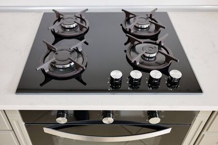 Modern built-in oven and gas stove classic design in dark tones under light stone marble or granite countertop, in interior of contemporary kitchen.の写真素材