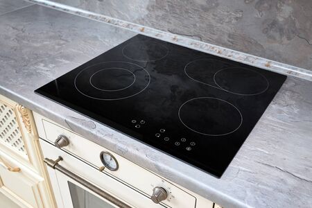 Modern kitchen interior with black induction or electric hob stove cooker with ceramic top surface with marble countertop and wall decorated with stoneの写真素材