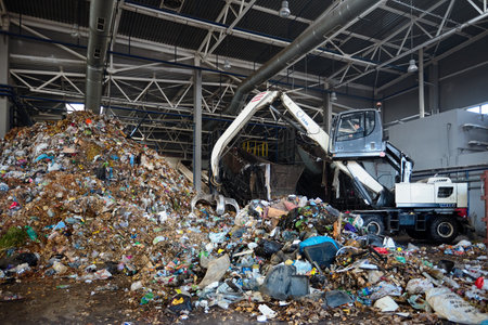 GRODNO, BELARUS - OCTOBER 2018: recycling plant process of uploading garbage to conveyor . Manipulator with grabber uploads waste on conveyor for further processing and sortingのeditorial素材