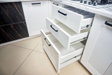 Solution for placing kitchen utensils in modern kitchen - horizontal sliding pullout drawer shelves storage in cupboard for kitchenware cookware under oak countertop gas hob, with copyspace.の写真素材