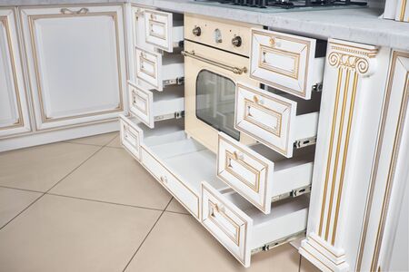 Interior of modern kitchen in classic antique style with golden elements in beige colors with wood facade panels, Lot of drawers and cupboards for plates or dishes shelf under countertop made of wood.の写真素材