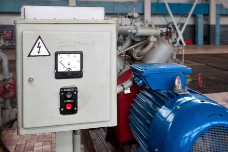 Start and Stop button for industrial machine closeup on electric control panel in chemical plant interior, near out of focus engine of pump or compressor. Concept of Emergency Stop for safety work.の写真素材