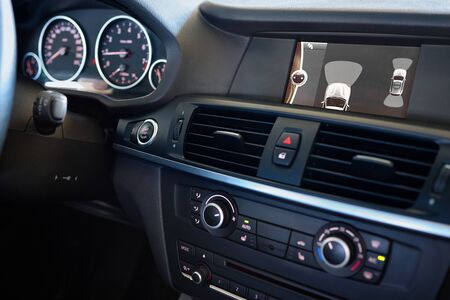 Premium car interior backup parking assistant system with sensors on screen with out of focus dashboard and steering wheel. Driver assistance system for parking, Help assist options inside luxury car.の写真素材