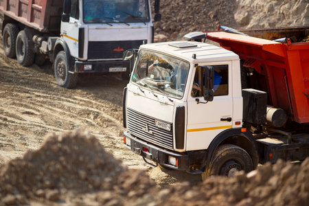GRODNO, BELARUS - APRIL 2020: Two heavy laden multi-ton trucks MAZ exporting minerals from open-pit mine. Concept of providing transport and freight for major construction projects. Selective focus.のeditorial素材