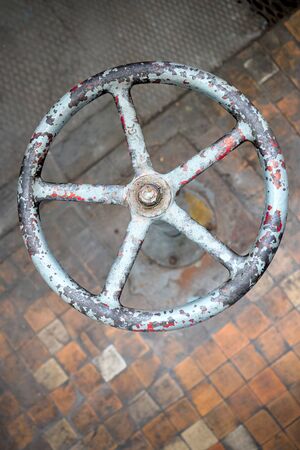 Old rusty valve wheel painted blue red with peeling selective focus with extension device over out of focus background tiled floor and perforated metal sheet stamping plates vertical, with copyspace.の写真素材