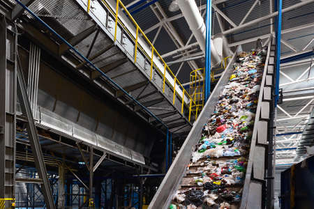 Conveyor belt with garbage transports waste inside drum filter or rotating cylindrical sieve with trommel for sorting pieces of garbage into various sizes fractions at waste recycling plant.の写真素材