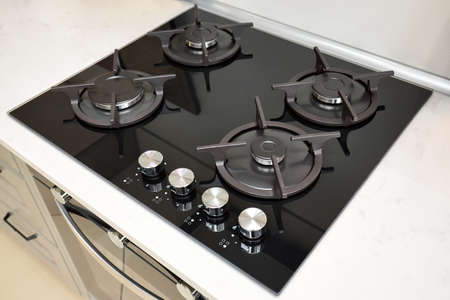 Hob cooker oven made of glass cast iron grill stainless steel control knobs selective focus over out of focus oven, with burner on countertop made of ceramic stoneware background.の写真素材