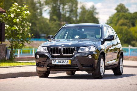 GRODNO, BELARUS - JUNE 2020: BMW X3 II F25 2.0i xDrive front three fourth view outdoors on sunny road background of summer city promenade flowering foliage landscape with copyspace.のeditorial素材