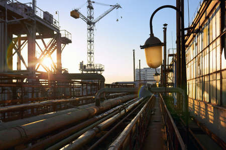 Lighting mast with selective focus explosion-proof and fireproof design lantern close-up over background of pipelines buildings and equipment of chemical plant with evening sunflares and copy space.の写真素材