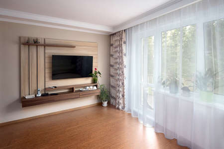 Modern apartment living room with large TV over wooden cabinet cork floorboards and glass door to balcony. Real room of real estate residential house.の写真素材