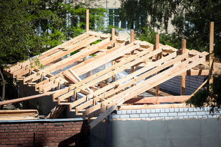 Roofing construction with wooden beams, logs, rafters, trusses. Roof structure on top of brick walls with plaster surrounded by foliage on sunny summer day top view.の写真素材