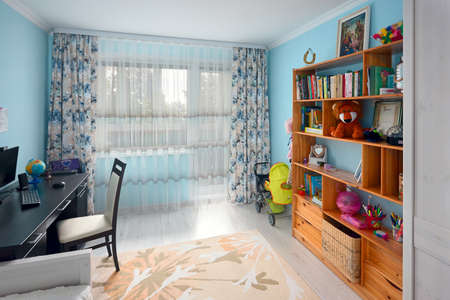 Cozy bright childrens room with blue walls pastel carpet on gray wooden floor wooden bookshelf bed and desk with globe and computer. Real estate apartment.の写真素材