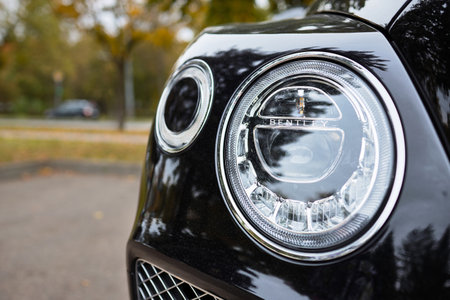 BERLIN, GERMANY - OCTOBER 2020: Bentley Bentayga Hybrid SUV luxury car parked on streets of Berlin in fall front view. Detail of car front light headlamp closeup on fall background with copyspace.のeditorial素材