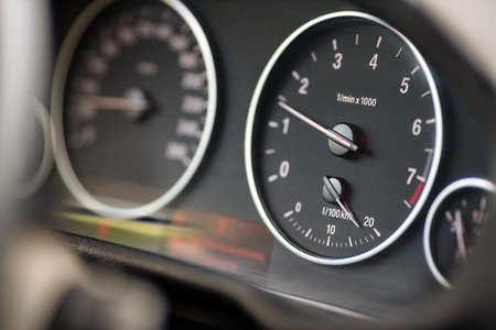 Rev counter of car selective focus closeup with copyspace. Tachometer or revolution counter, RPM gauge with red glowing needle on car dashboard with fuel and out of focus speed meter.の写真素材